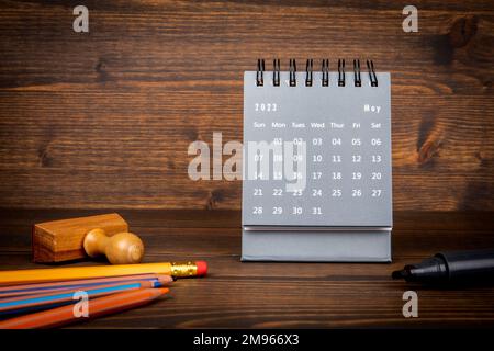 2023. Mai. Schreibtischkalender und Bürobedarf auf strukturiertem Holzhintergrund. Stockfoto