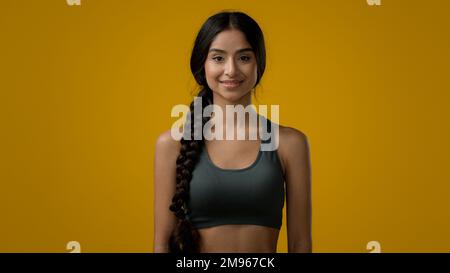 Ethnisch fröhlich lächelnde 20s Frau Indische Sportlerin multirassisch stark schlanke Sportlerin in gelbem Studioathleten weiblich Look Stockfoto