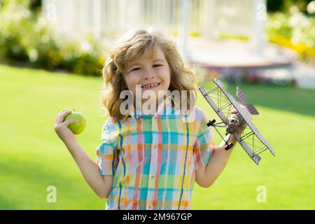 Ein Kind im Dorf mit einem Flugzeug in der Hand. Kind Junge Kleinkind spielt mit Spielzeugflugzeugflügeln und träumt von der Zukunft. Der Begriff der Kindheit und Stockfoto