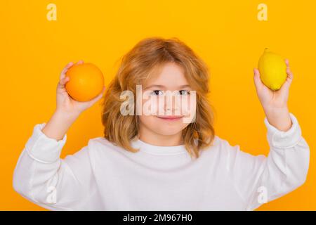 Ein Junge mit Orange und Zitrone im Studio. Studioporträt mit süßem Kinderhalter, Zitrone und Orange isoliert auf gelbem Hintergrund. Stockfoto