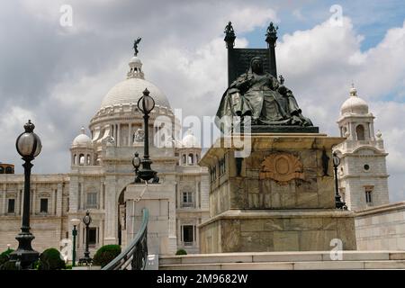 Das Victoria Memorial in Kalkutta, Indien, mit einer Statue im Vordergrund von Königin Victoria auf einem Thron. Die Gedenkstätte wurde zwischen 1906 und 1921 zum Gedenken an Königin Victoria von Großbritannien und Kaiserin von Indien erbaut. Es ist jetzt ein Museum. Stockfoto