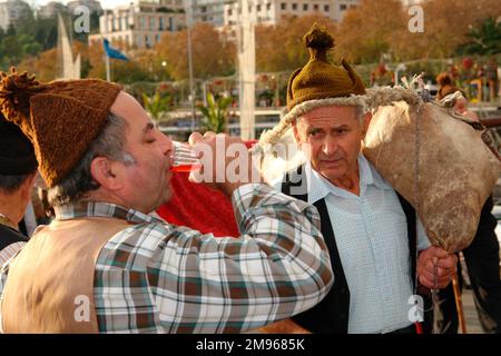 Zwei Männer, die einer Folkloregruppe von Porto da Cruz angehören, nehmen an Straßenunterhaltung in Funchal, der Hauptstadt von Madeira, Teil. Der Mann auf der rechten Seite trägt Wein in einem Weinkeller über seine Schulter, während der Mann auf der linken Seite einen schnellen Schluck genießt. Stockfoto