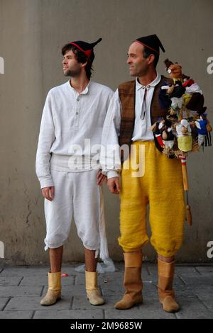 Zwei junge Männer, die einer Machico-Folkloregruppe angehören, tragen traditionelle Kostüme. Der Mann auf der rechten Seite hält ein Musikinstrument, das Brinquinho genannt wird, einen Stock, der mit Holzpuppen, Glocken und Kastanien dekoriert ist, der auf und ab geschüttelt wird, damit die Gruppe herumtanzen kann. Sie nehmen an Straßenunterhaltung in Funchal, der Hauptstadt von Madeira, Teil. Stockfoto