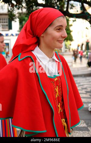 Eine junge Frau aus einer Folklore-Gruppe von Gaula, trägt ein traditionelles Kostüm, bestehend aus einem leuchtend roten Umhang, Kleid und Kopftuch. Sie ist in Funchal, der Hauptstadt von Madeira, und nimmt an Straßenunterhaltung Teil. Stockfoto