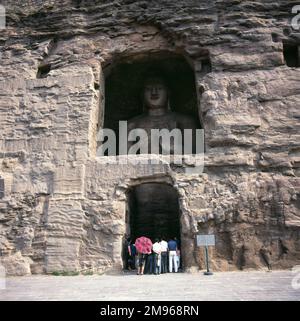 Besucher, die die Buddha-Statue in Yungang (Cloud Ridge) Cave oder Grotto No 18 in Datong, Provinz Shanxi, Volksrepublik China. Stockfoto