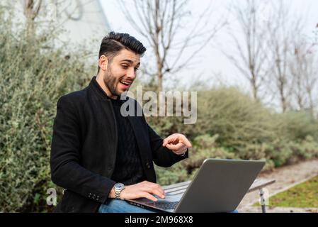 Junger Geschäftsmann, der im Außenbereich an einem Notebook arbeitet, mit grüner Natur im Hintergrund, Geschäftskonzept, Freiheit und Lebensstil für Telearbeit Stockfoto