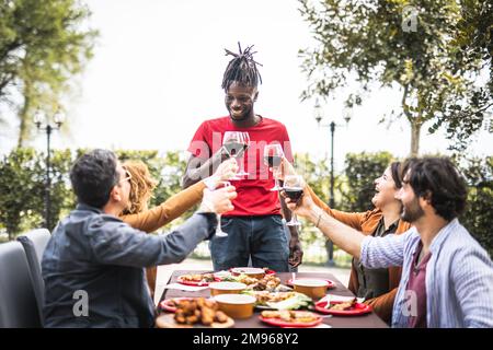 Fröhliche Familie jubelt mit Rotwein beim Barbecue-Mittagessen im Freien, verschiedene Altersgruppen, die Spaß beim Wochenendessen haben, Essen, Geschmack und Familienkonzept, foc Stockfoto