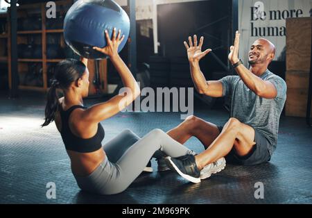 Es ist ein lustiges Workout, das Sie gemeinsam genießen können. Ein sportlicher junger Mann und eine sportliche Frau, die zusammen mit einem Medizinball in einem Fitnessstudio trainieren. Stockfoto