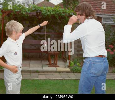 Ein Junge und ein junger Mann, die im Garten Conker spielen. Der Junge hält sein Konker fest, damit der Mann zuschlagen kann. Stockfoto