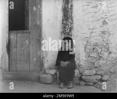 Eine alte Frau in Schwarz, die auf einem Stein vor ihrem Haus sitzt, vielleicht in Spanien. Stockfoto