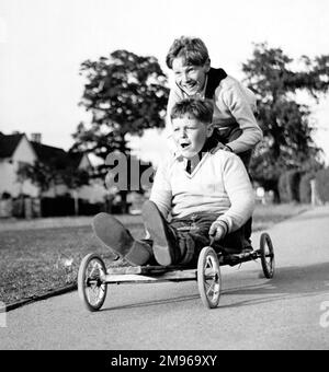 Zwei Jungs genießen eine Fahrt in einem hausgemachten Go-Kart in Horley, Surrey. Stockfoto