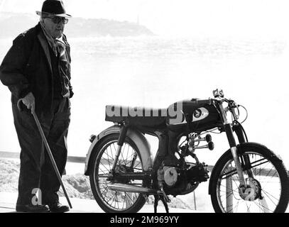 Ein alter Mann mit einem Gehstock, der neben einem Motorrad steht, das in der Nähe eines Strandes geparkt ist. Stockfoto