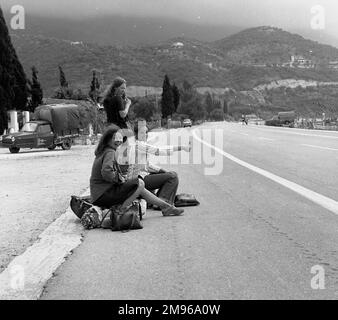 Drei junge Frauen trampen am Straßenrand in Ipsos, Korfu, Griechenland. Stockfoto