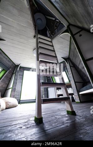 Weiße senkrechte Holztreppe zum zweiten Stock vom Wohnzimmer des Sommerhauses. Pyramidenförmiger Bungalow von innen. Fußbodenwände Decken Treppen verrückt Stockfoto