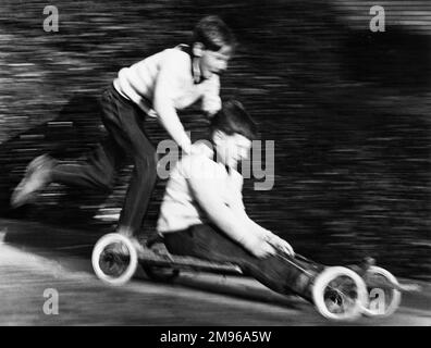 Zwei Jungs genießen eine Fahrt in einem hausgemachten Go-Kart in Horley, Surrey. Sie fahren so schnell, dass das Foto verschwommen ist! Stockfoto