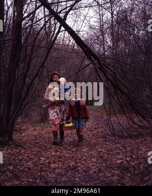 Eine Zigeunermutter und zwei Töchter, Mitglieder der Familie Vincent, wandern durch einen Wald in der Newdigate Gegend von Charlwood, Surrey. Sie tragen bunte Kleidung und tragen gelbe Blumen. Stockfoto