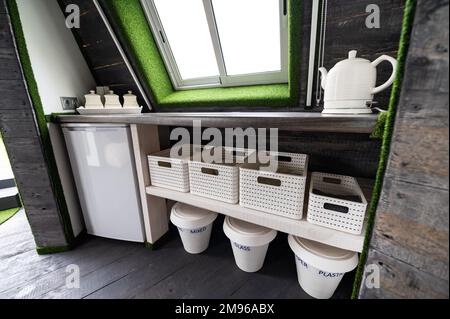 Kleine Küchenelemente in einem Holzsommerhaus. Kühlschrank, Wasserkocher, heiße Getränke, Geschirr und Recyclingdosen in einer kleinen Küche. Originell, ungewöhnlich, vielleicht Stockfoto
