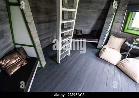 Weiße senkrechte Holztreppe zum zweiten Stock vom Wohnzimmer des Sommerhauses. Pyramidenförmiger Bungalow von innen. Fußbodenwände Decken Treppen verrückt Stockfoto