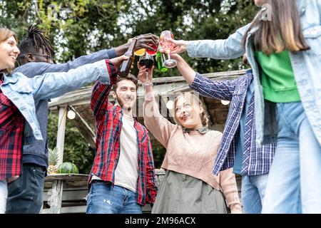 Fröhliche multiethnische Menschen, die Spaß auf einer Familienfeier auf dem Dach haben, während sie ein Getränk in der Chiringuito Bar trinken, multikulturelle Freunde feiern die Geburt Stockfoto