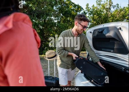 Glückliches Paar junger Reisender, die vor der Abreise den Kofferraum beladen haben, Valentinsliebhaber, die reisen Stockfoto