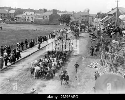 Straßenszene, die einen Teil der Sanger's Circus Parade bei einem Besuch in Haverfordwest, Pembrokeshire, Dyfed, South Wales zeigt, mit mehreren aufwendigen Pferdekutschen und Reitern in schicken Kostümen. Die Leute auf dem Bürgersteig halten an und schauen nach, und ein paar Jungs folgen auf der Straße. Einige Leute sitzen auf einem alten, mit Gras bedeckten Limofen (rechts). Sanger war ein berühmter Zirkusimpresario, der seit den 1850er Jahren spektakuläre Shows an großen Veranstaltungsorten im ganzen Land veranstaltete. Stockfoto