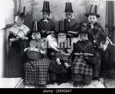 Eine Gruppe von sieben walisischen Mädchen in traditionellen Kostümen. Eine von ihnen hält eine große Puppe auf ihrem Schoß, und drei halten Körbe. Stockfoto