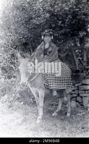 Eine junge walisische Frau in traditionellem Kostüm, die auf einem Eselsattel reitet. Das war damals die übliche Transportart – zum Beispiel waren Mädchen und Frauen dafür bekannt, von Hook nach Haverfordwest zu reisen, um dort zu arbeiten, eine Entfernung von drei oder vier Meilen. Stockfoto