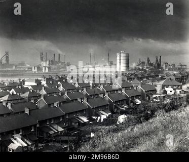 View of the BSC (British Steel Corporation) arbeitet in Port Talbot, West Glamorgan, Südwales, mit Reihen von Häusern im Vordergrund. Über der Stadt hängt eine dunkle Verschmutzungswolke mit Rauch aus den Schornsteinen. Stockfoto