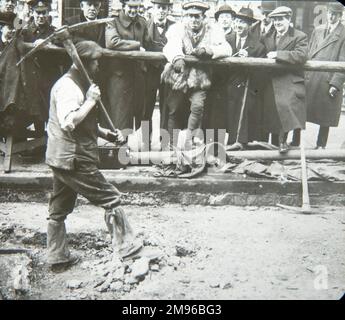 Eine Gruppe amerikanischer Servicemitarbeiter, zusammen mit ein paar Zivilisten, beobachtet einen Mann bei Straßenreparaturen im Zweiten Weltkrieg. Stockfoto