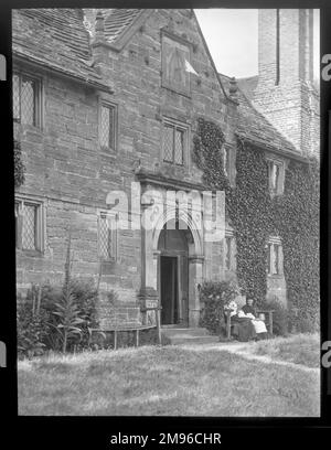 Außenansicht des Sackville College, East Grinstead, West Sussex, ein jakobinisches Altenhaus, das 1609 gegründet wurde, um geschützte Unterkünfte für ältere Menschen zu bieten. Zwei ältere Frauen sitzen auf einer Bank rechts neben der Tür. Stockfoto