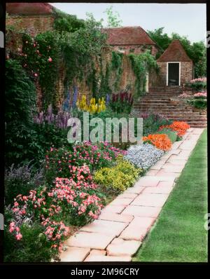 Blick auf den ummauerten Garten auf der Rückseite der Great Maytham Hall, einem denkmalgeschützten Landhaus der Kategorie II in der Nähe von Rolvenden, Kent. Es war die Inspiration für den Kinderklassiker, den Secret Garden, von Frances Hodgson Burnett, der dort zwischen 1898 und 1907 lebte. Burnett restaurierte den vernachlässigten Garten und pflanzte Hunderte von Rosen. Hier sehen Sie eine Reihe von Blumen an der Seite eines Weges, mit einer Treppe oben. Stockfoto