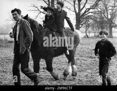 Ein Zigeuner und drei Jungen mit ihrem Pferd. Der Mann führt das Pferd über ein eisiges Feld. Zwei Jungs reiten auf dem Rücken des Pferdes, und ein dritter Junge läuft nebenan. Stockfoto