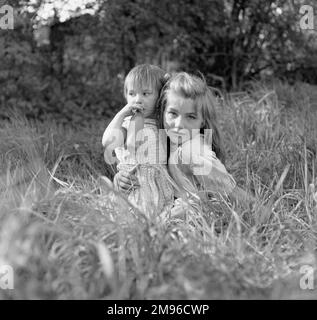 Zwei Zigeunermädchen, die auf einem Feld im Gras sitzen. Das jüngere Mädchen hält eine Flasche an den Mund. Stockfoto