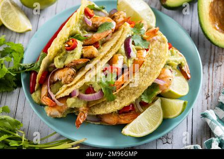 Mexikanische Tacos mit Garnelen, Guacamole und Gemüse auf einem Holztisch Stockfoto