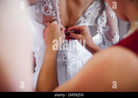 Freundinnen schnüren weiße Kleidung die Braut auf dem Korsett am Hochzeitstag im Hotel Stockfoto