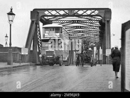 Zwei Verkehrsmittel auf einer Londoner Brücke -- ein Doppeldeckerbus auf der linken Seite, ein Pferdewagen auf der rechten Seite. Der Bus fährt auf der Route 33A nach Sheen, Hammersmith, Kensington, Piccadilly Circus, Charing Cross und The Strand. Auf einem Schild steht: Gefahr, kein Durchgang für Fußgänger. Stockfoto