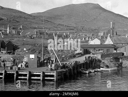 Eine Wasserszene in Schottland mit einem Steg, Häusern und einer Kirche. Fässer sind links aneinander gestapelt. Stockfoto