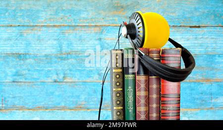 Hörbuchkonzept mit Bücherreihe und klassischen Kopfhörern, verwischte blaue Holzplanken im Hintergrund Stockfoto