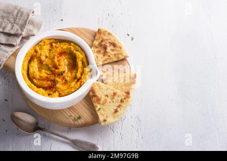 Köstlicher gesunder hausgemachter Bohnenhummus mit gebackenem Kürbis, Tahina und Gewürzen mit flachem Brot auf hellblauem Hintergrund, Blick von oben, Platz Stockfoto