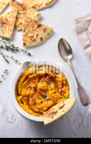 Köstlicher gesunder hausgemachter Bohnenhummus mit gebackenem Kürbis, Tahina und Gewürzen mit flachem Brot auf hellblauem Hintergrund, Draufsicht Stockfoto