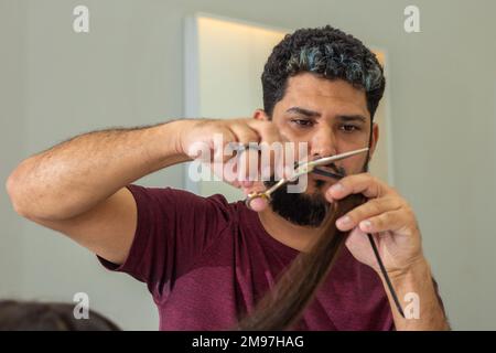 Goiania, Goiás, Brasilien – 10. Januar 2023: Ein Friseur, der die Haarspitzen eines Kunden mit einer Schere schneidet. Stockfoto