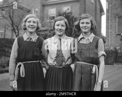 Drei lächelnde Mädchen in Schuluniform in einem Garten. Stockfoto