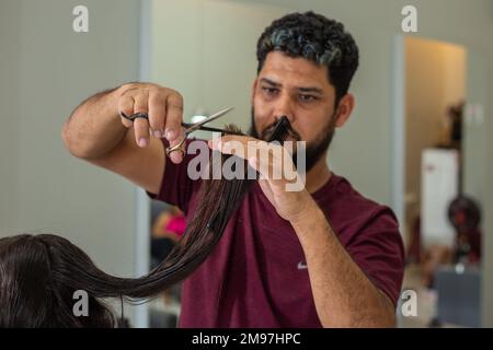 Goiania, Goiás, Brasilien – 10. Januar 2023: Ein Friseur, der die Haarspitzen eines Kunden mit einer Schere schneidet. Stockfoto