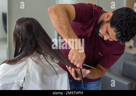 Goiania, Goiás, Brasilien – 10. Januar 2023: Ein Friseur, der die Haarspitzen eines Kunden mit einer Schere schneidet. Stockfoto