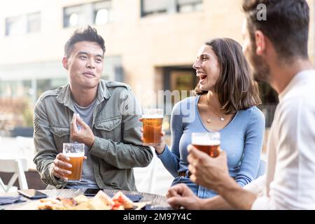 Multirassische Freunde trinken Bier im Biergarten der Brauerei - echtes Freundschaftsleben Konzept mit Jungs und Mädchen genießen Happy Hour Essen zusammen Stockfoto