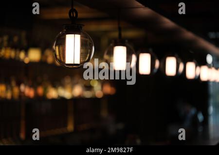 Eine Reihe von Pendelleuchten in der dunklen Café-Bar mit farbenfrohem Bokeh Stockfoto