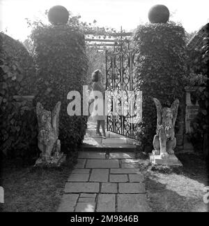 Schmiedeeisentor in einem Garten mit weiblichem Modell. Stockfoto