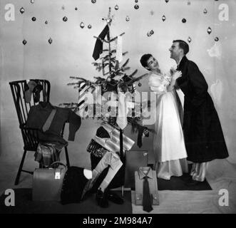 Männliche und weibliche Models in einer Weihnachtsmorgenszene mit Baum und Geschenken. Stockfoto