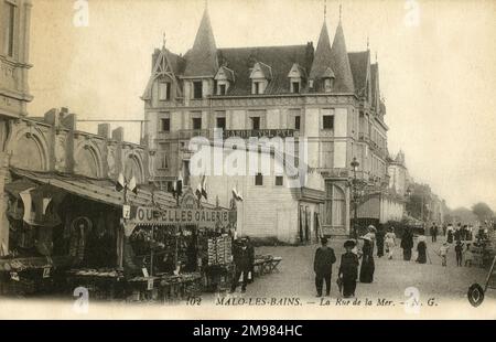 Malo-les-Bains, Frankreich - die Küstenstraße (Rue de la Mer) der Strandstadt Malo-les-Bains in der Nähe von Dünkirchen in Nordfrankreich. Hinter den Leuten, die die Straße hoch laufen, befinden sich ein großes Hotel (Grand Hotel Pyl) und Marktstände. Stockfoto