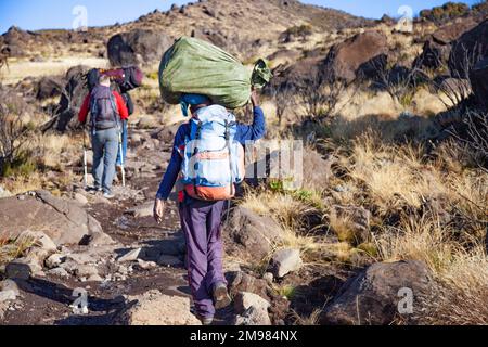 Ein Portier, der schwere Lasten auf dem Rücken trägt, läuft die Straße entlang. Stockfoto